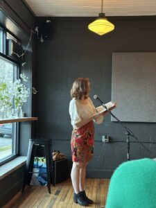 Marianne Erhardt standing in front of a microphone reading from her book.